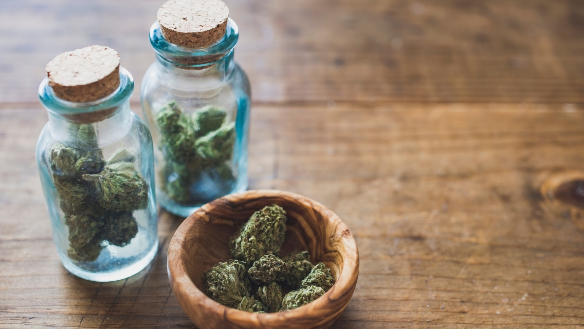 small jars with cannabis inside. next to a bowl with cannabis in it. wood background