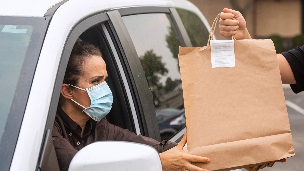 a woman wearing a mask grabs her bag, accepting her curbside pickup order.